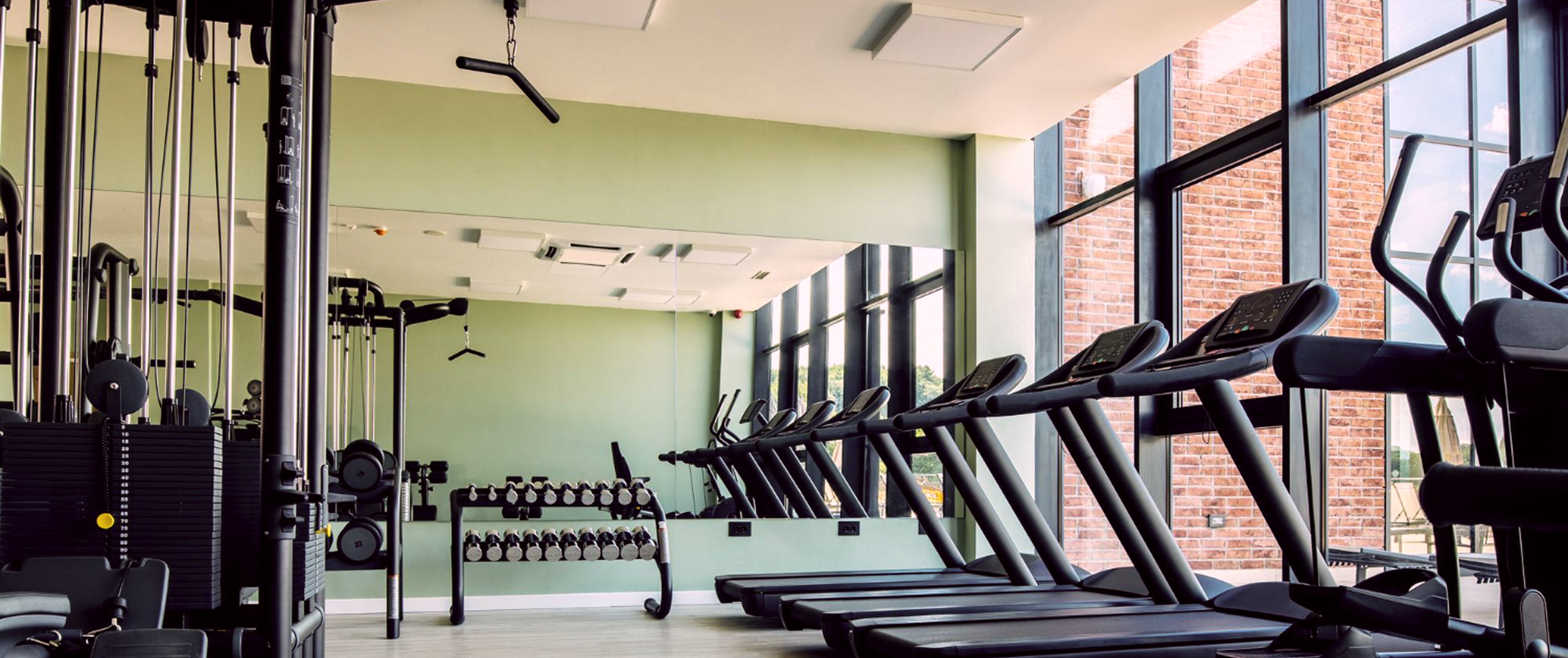 На фотографии просторный зал, оборудованный различными агрегатами для качалки, с панорамными окнами, наверняка выходящими на суетный город